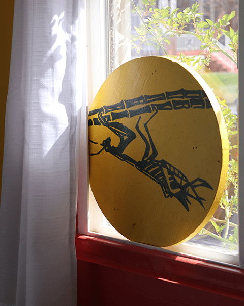 circlular painting of green mantis on yellow in window sil